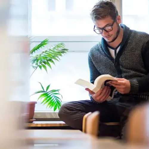 Young man reading a book in library