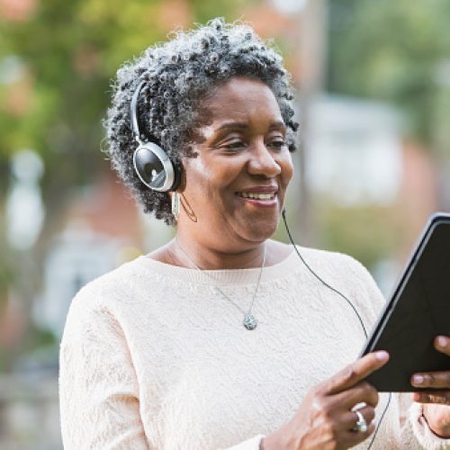 Close up of a senior, African American woman wearing headphones and using a digital tablet.  She could be listening to music or an audio book.