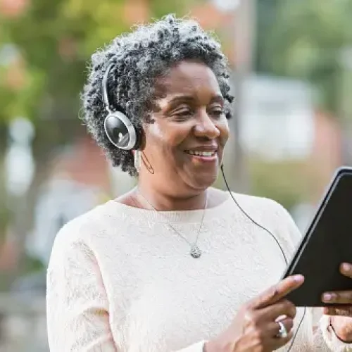 gettyimages-538685563-170667a Close up of a senior, African American woman wearing headphones and using a digital tablet. She could be listening to music or an audio book.